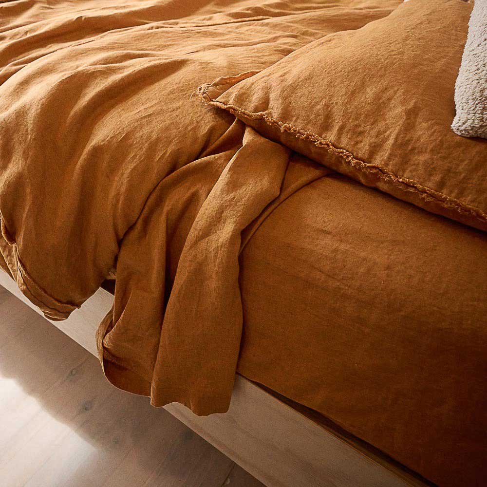 A bed with sophisticated flax linen sheets in shades of warm, monochromatic orange. 