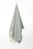 Palliser Ridge Herringbone throw in Forest hanging in full drape, showing the fringed edge