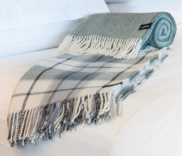 Palliser Ridge Twill Check lambswool throw in Forest, rolled on a bed showing the check pattern and plain reverse side