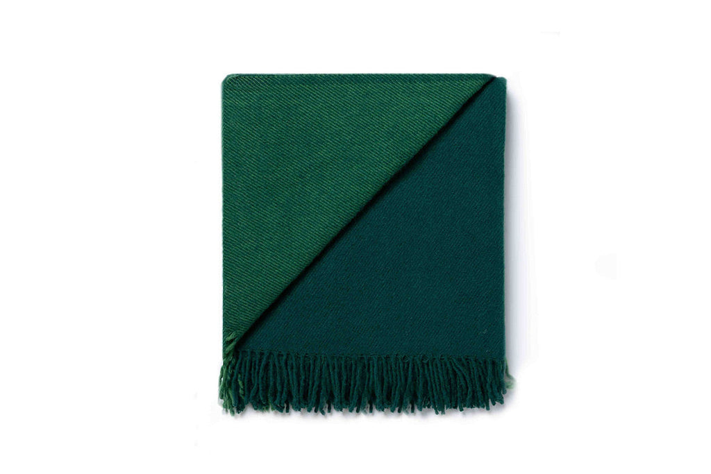 A folded green throw blanket by Ruanui Station NZ, folded back on itself to show the differentiation in tones of the wool. 