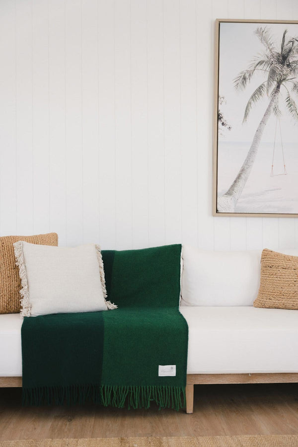 A deep green lambswool throw blanket by Ruanui Station, thrown over the back of a white couch. 