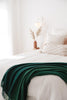 A stylish bedroom, with a green throw blanket by Ruanui Station NZ draped over the end of the bed. 