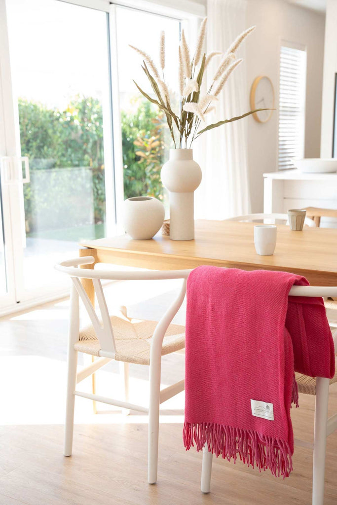 A modern dining room, with a pink throw blanket by Ruanui Station NZ folded over the side of one of the chairs. 