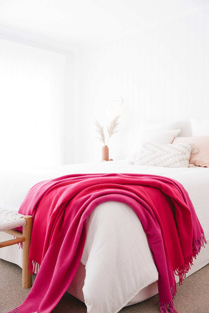 A stylish bedroom, with a pink throw blanket by Ruanui Station NZ draped over the end of the bed. 