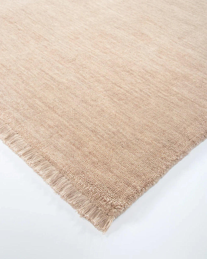 Corner of the Baya Sandringham wool rug in blush pink 'Cameo' colour, with small tasseled edge