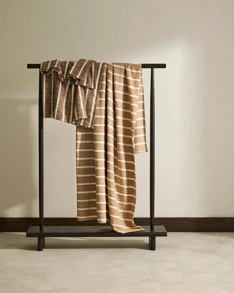 A hanging rack containing two Piazza throws by Weave Home, in the shades Earth and Haze. 