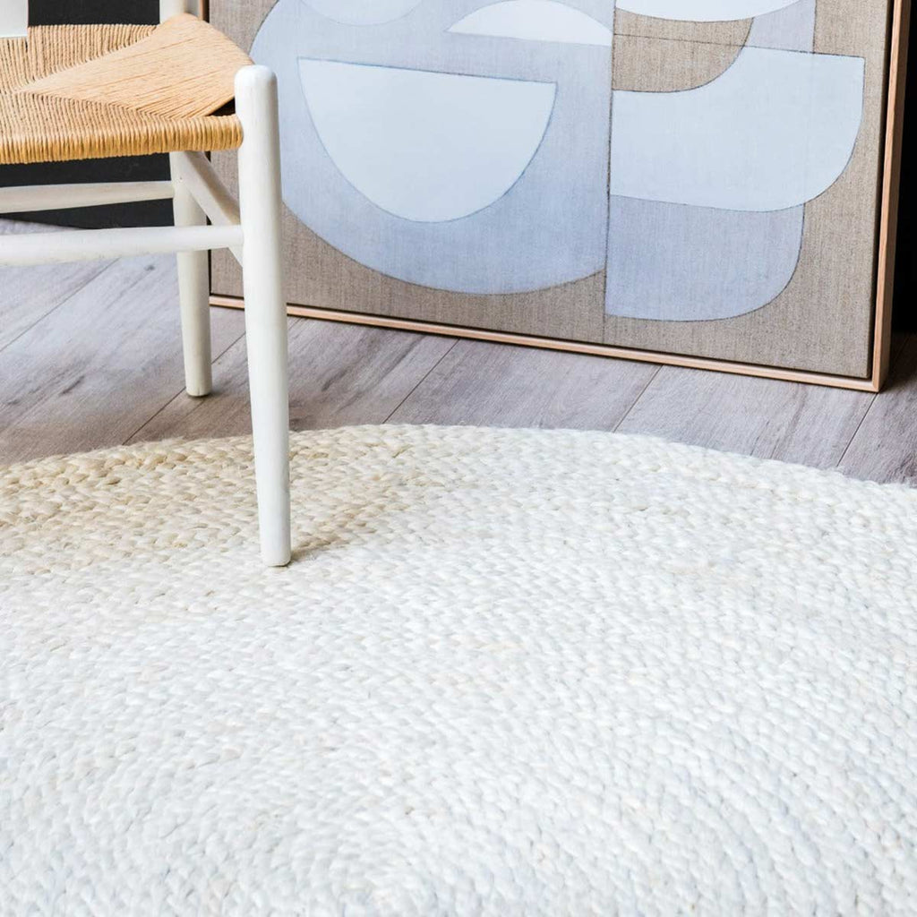 A hand braided jute floor rug in white, in a dining room in neutral tones. 