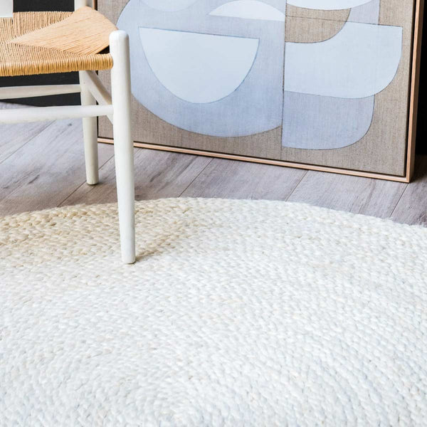 A hand braided jute floor rug in white, in a dining room in neutral tones. 