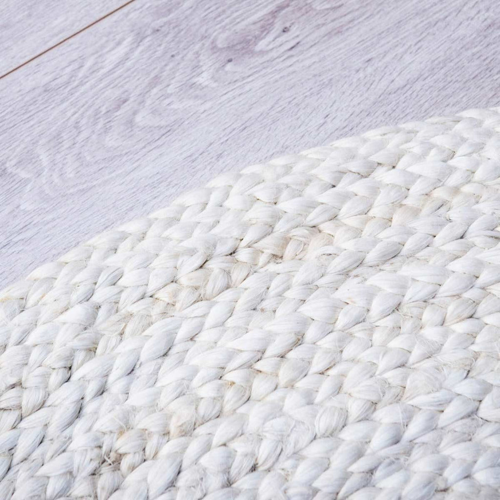 A close up of the edge of a braided jute white washed round floor rug. 