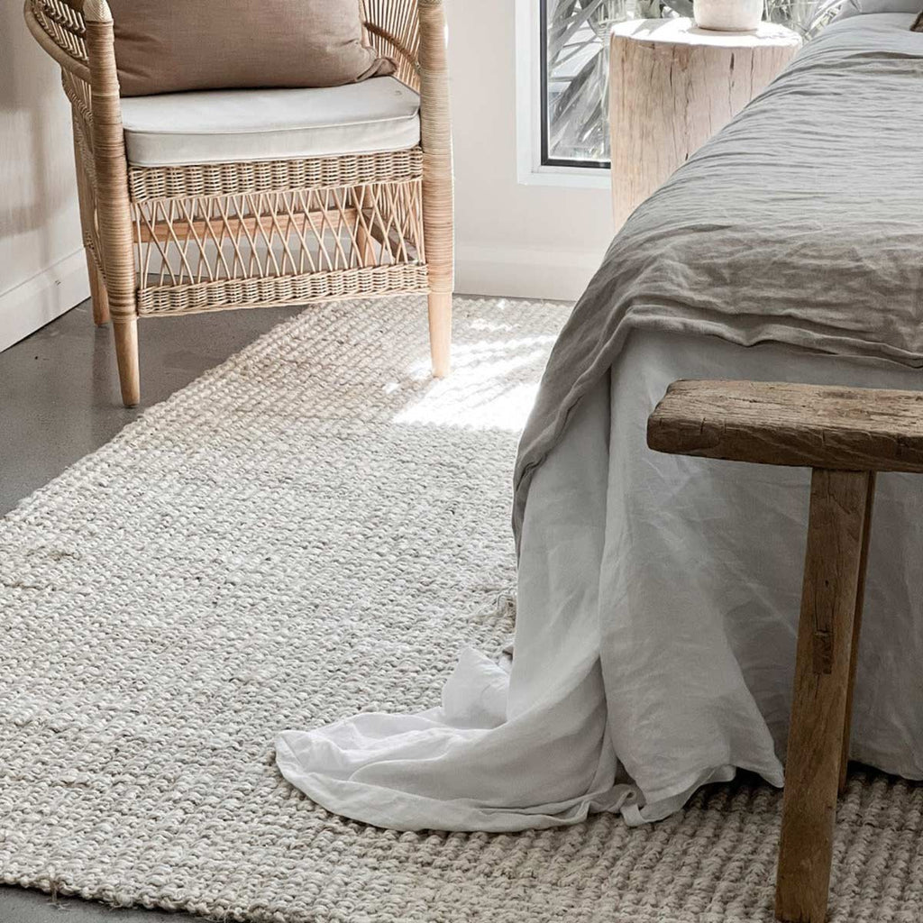 A soft and cosy bedroom in neutral tones with a white floor rug in jute and a boucle weave. 
