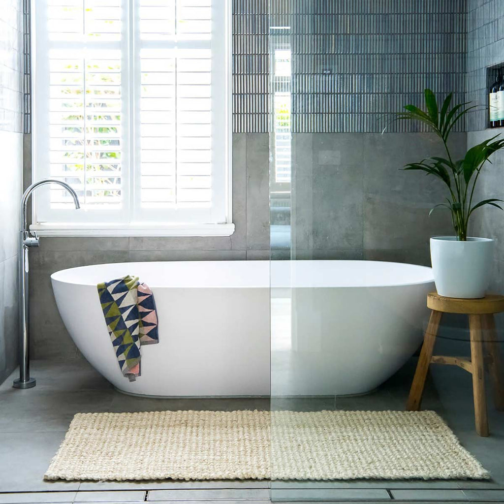 A bathroom with an oversized white jute floor mat just outside the bath. 
