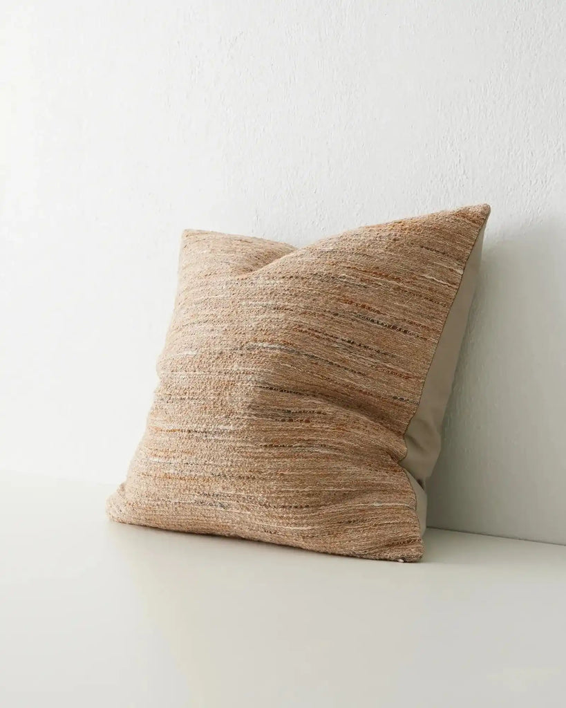 Th 'Vista Sunset' cushion featuring a texturla weave in warm brown colours,seen on an angle to reveal the reverse