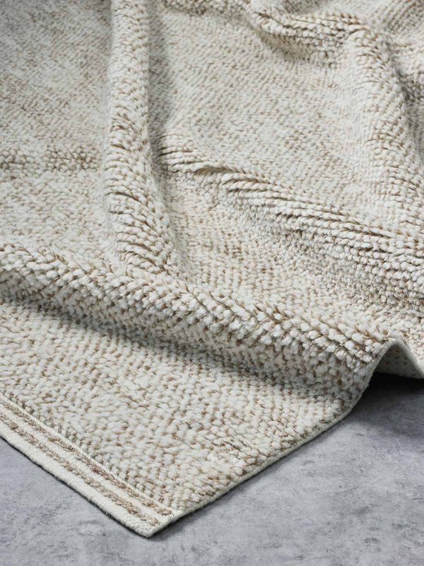 A luxurious, deep-cut pile floor rug in 100% NZ wool made by Tribe Home. A soft ivory colour offset with flashes of ginger, orange, and brown, with the depth of the pile offset by a linear border. 