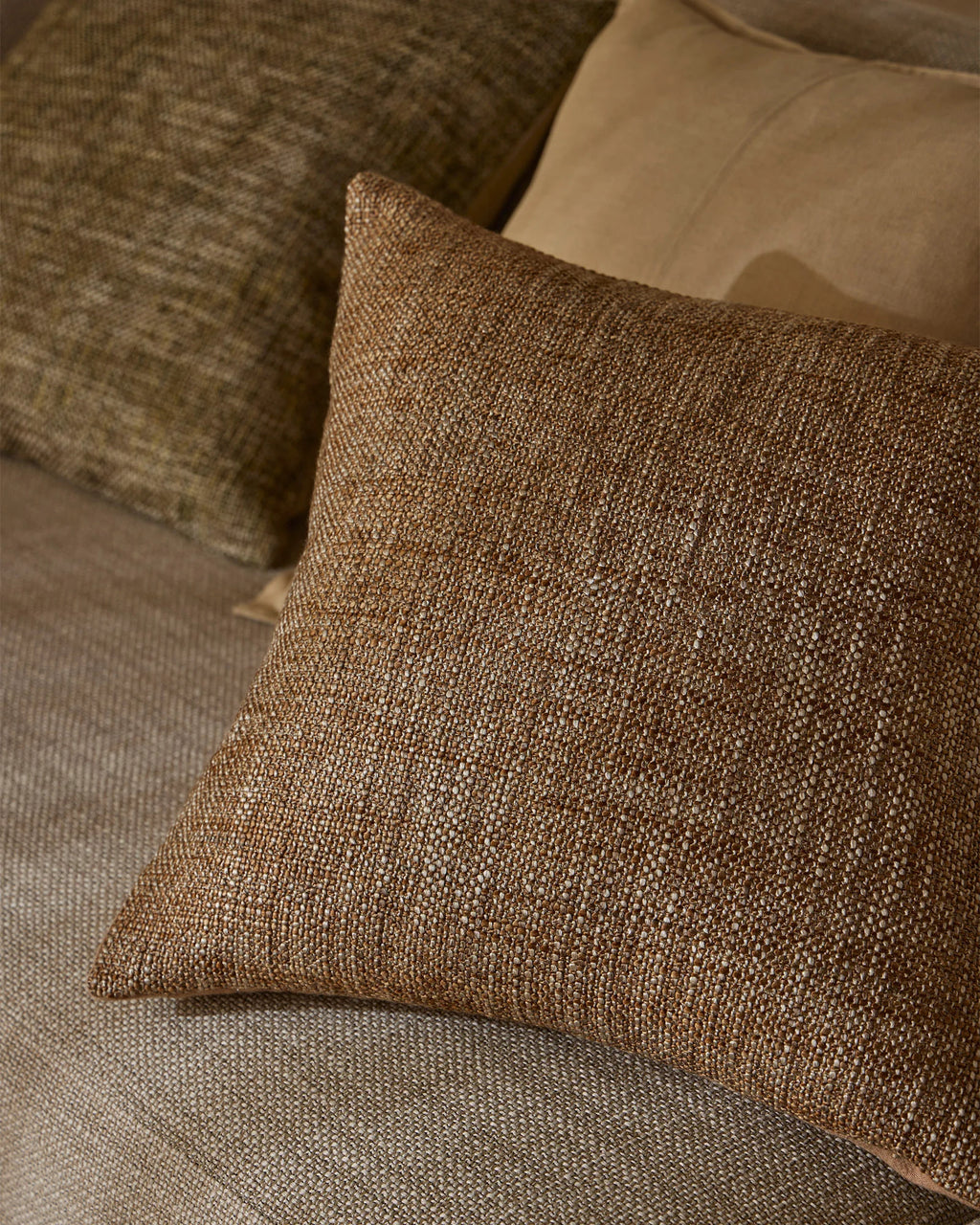 Weave Home Castel cushion in Auburn layered with olive and tan cushions.