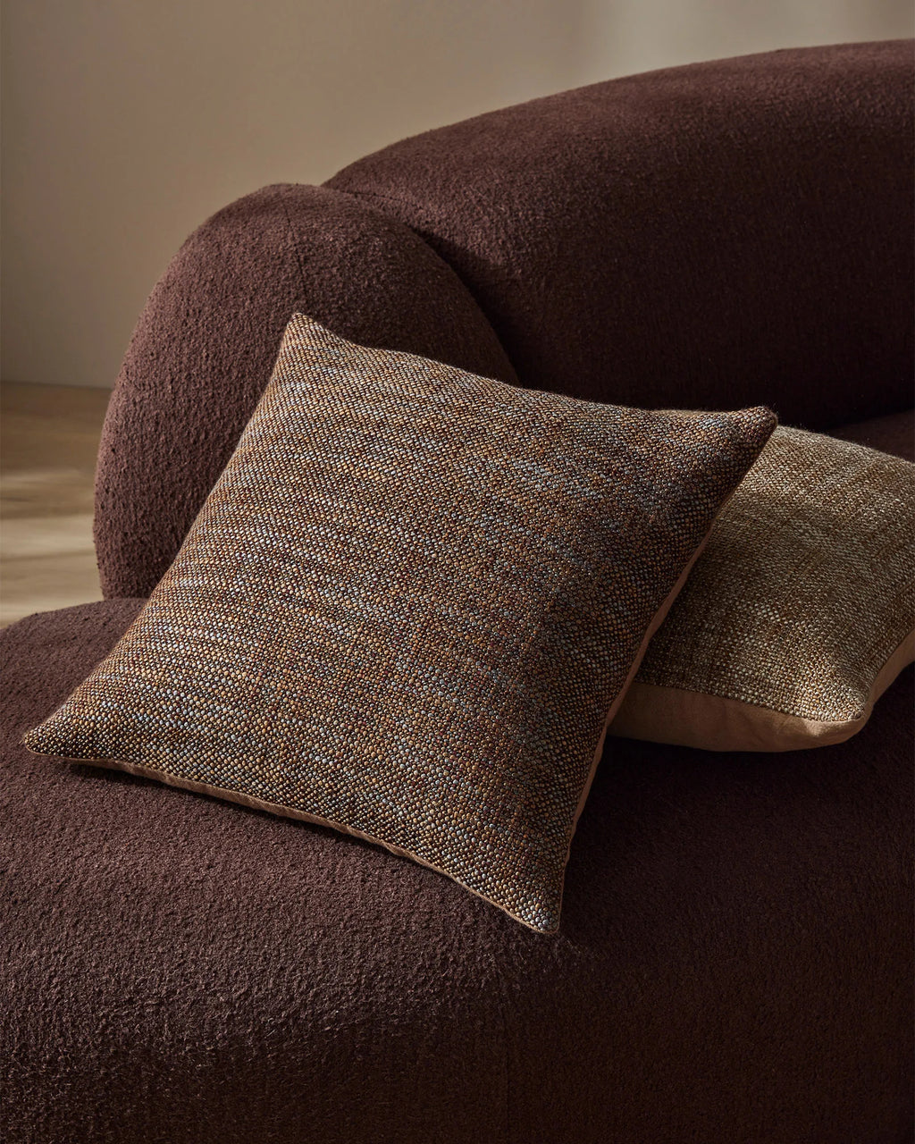 Weave Home Castel cushion in Auburn on a curved brown sofa.