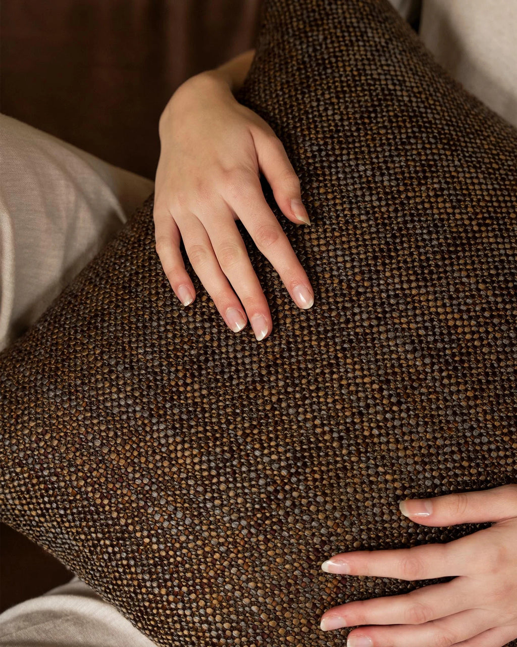 Hands resting on the woven texture of the Weave Home Castel cushion in Auburn.
