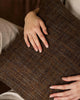 Hands resting on the woven texture of the Weave Home Castel cushion in Auburn.
