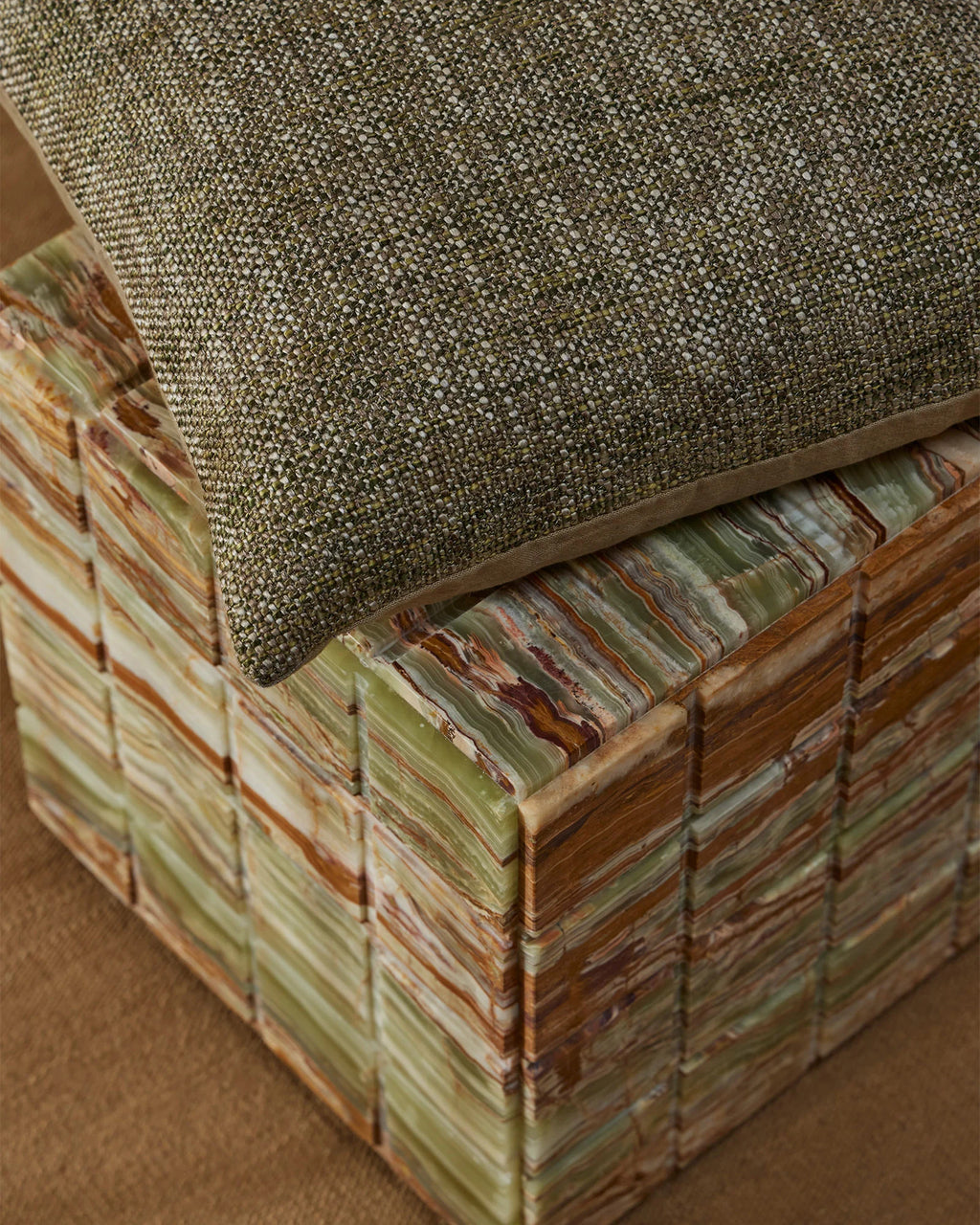 Weave Home Castel cushion in Moss resting on a striped stone bench.