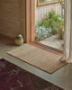 Weave Home Ivano jute doormat in Wheat styled at a timber entranceway.