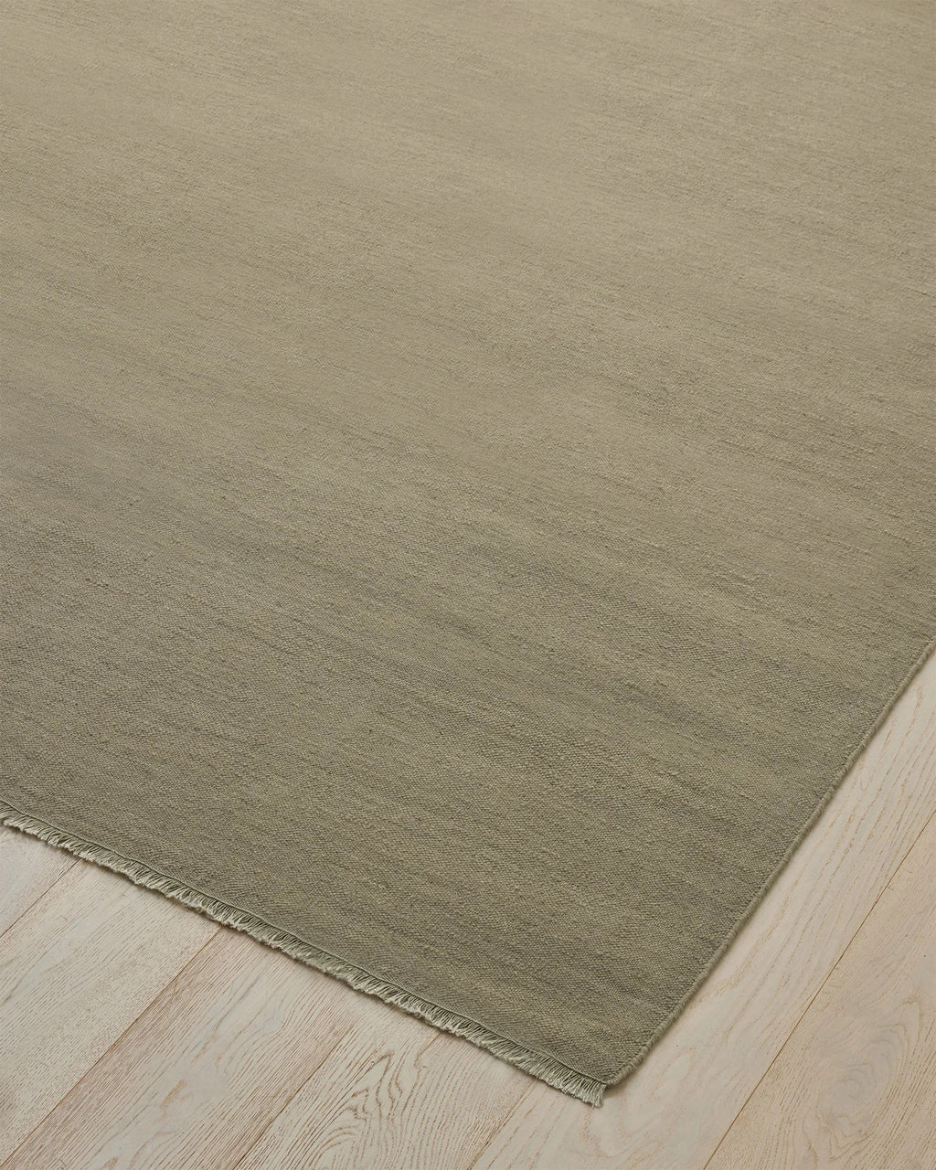 Weave Home Jacqueline wool rug in Pumice on a pale timber floor, showing the fringed corner
