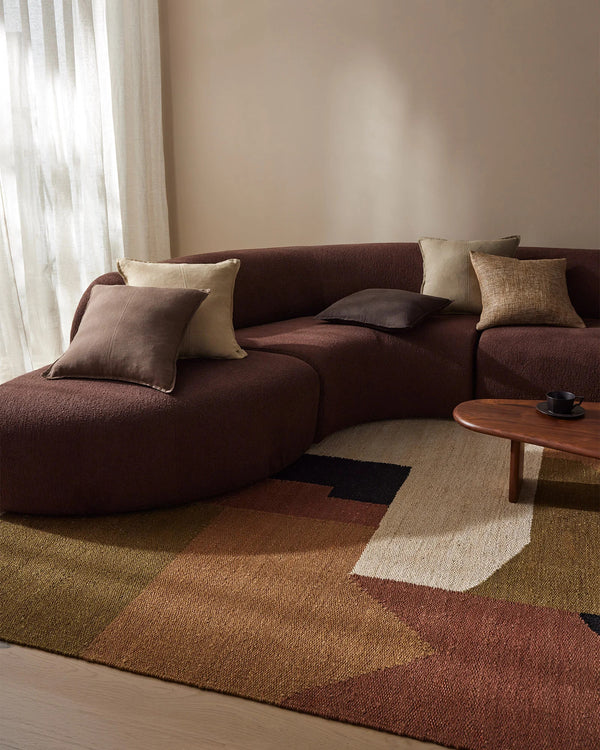 Weave Home Ruben jute rug in Terra beneath a curved sofa and round timber coffee table