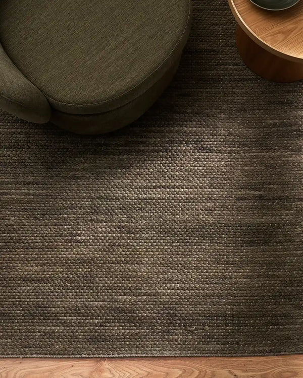 Baya khaki green wool-blend floor rug under a chair and table in a contemporary living room