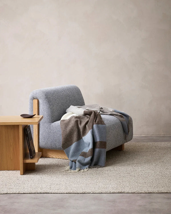 The Baya nz wool throw blanket in soft blues and browns, with tasseled fringe, in a contemporary living room