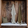 The Zen throw blanket hanging up in an alcove, the olive-green of the knit contrasting beautifully with the dark wood of the wall. 