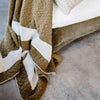 The corner of the Zen throw blanket, featuring a stark creamy white stripe and olive textural cotton knit. 